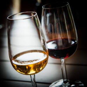 Zwei Weingläser stehen nebeneinander auf einem Tisch, eines mit Weißwein, das andere mit Rotwein. Die Gläser reflektieren das Licht und heben die Farben und die Klarheit der Weine hervor - die perfekte Ergänzung zu einem Käsebuffet.