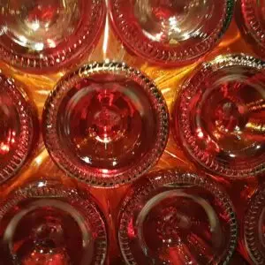 Nahaufnahme der Böden mehrerer Glasflaschen von Weinland, die in einem Gittermuster angeordnet sind und mit warmen Rot- und Orangetönen beleuchtet werden, wodurch ein leuchtender, abstrakter Effekt entsteht. Think Pink Vibes bilden den Rahmen für den 18.09.2026.